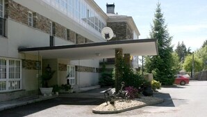 Un hotel con entrada cubierta, fachada de piedra y un aparcamiento con un coche rojo.