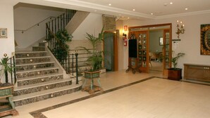Un vestíbulo de hotel con una escalera de mármol, una recepción y un área de comedor.