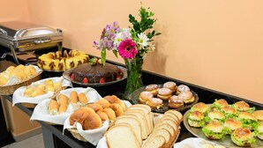 Una mesa de buffet con diversas opciones de comida, incluyendo pan, bollería y un pastel de chocolate.