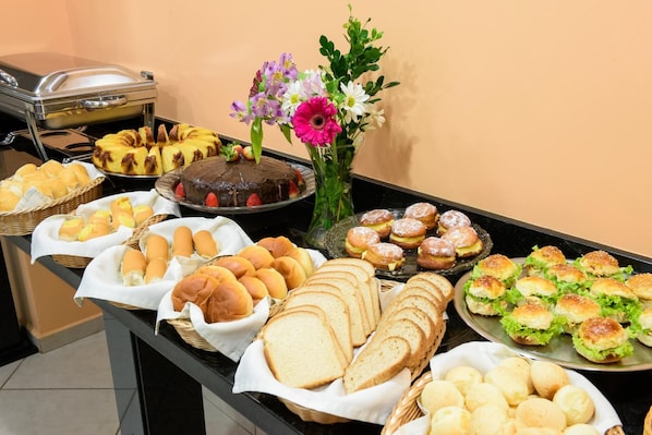Una mesa de buffet con diversas opciones de comida, incluyendo pan, bollería y un pastel de chocolate.
