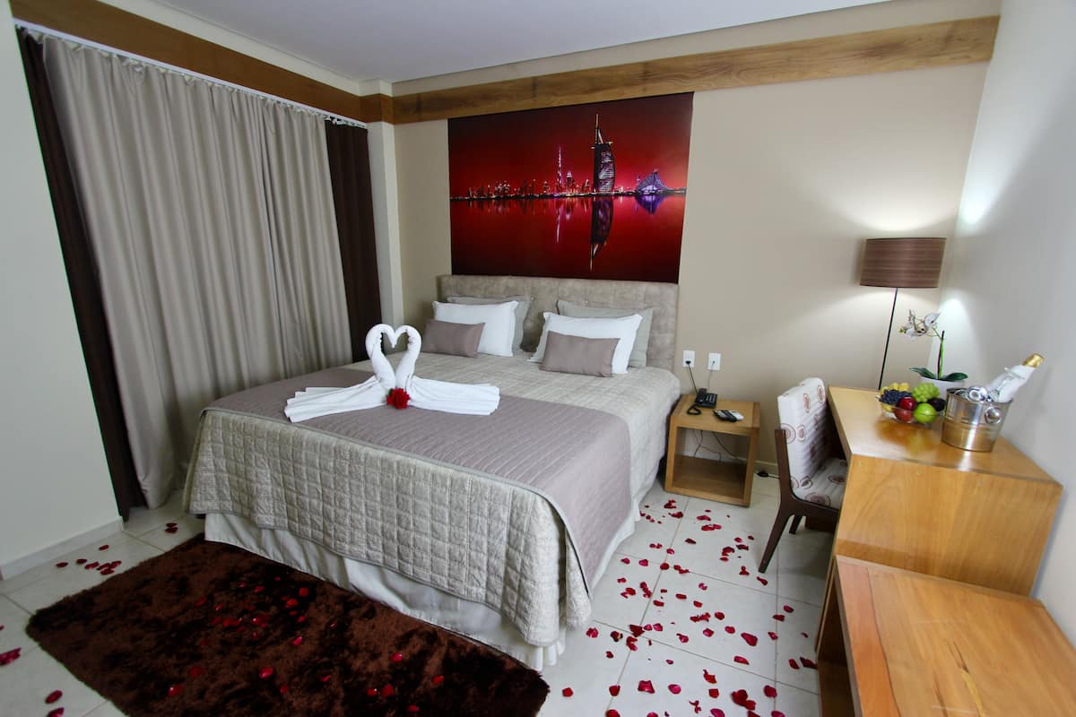 Habitación de hotel con una cama grande, un escritorio, una silla, una mesita de noche y un cuadro de un horizonte urbano.