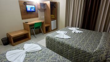 A hotel room with two beds, a desk with a computer, a small refrigerator, and a green chair.