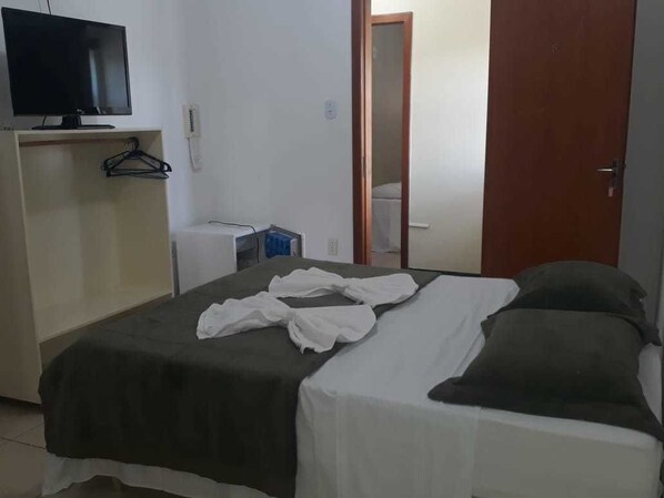 A bedroom with a bed, a television on a stand, a wardrobe, and a door leading to another room.