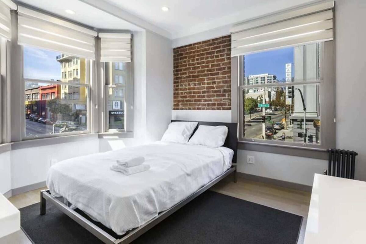 Ein modernes Hotelzimmer mit einem großen Bett, einer Wand aus Ziegelsteinen und großen Fenstern mit Blick auf die Stadt.