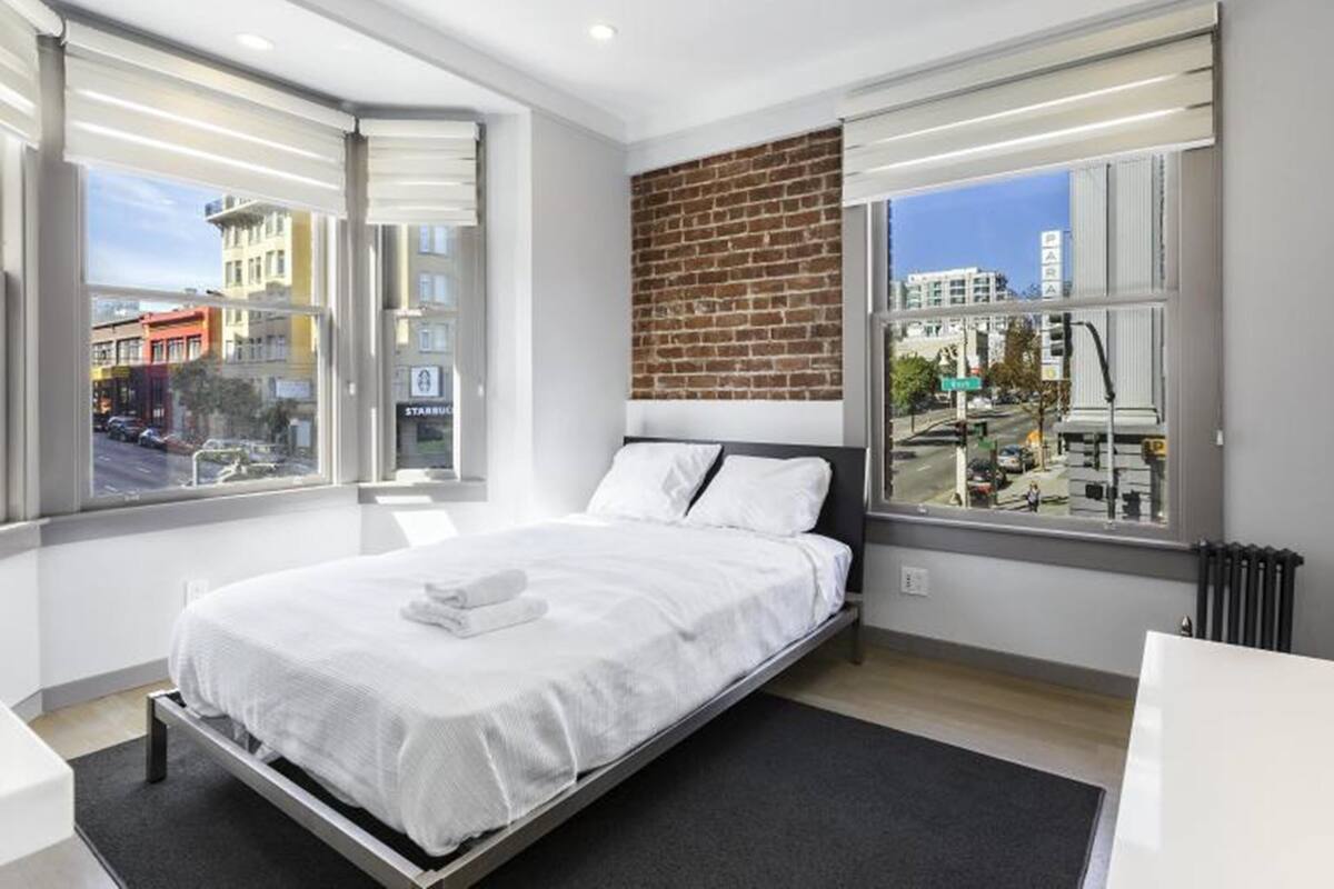 Ein modernes Hotelzimmer mit einem großen Bett, einer Wand mit Backsteinverkleidung und großen Fenstern mit Blick auf die Stadt.