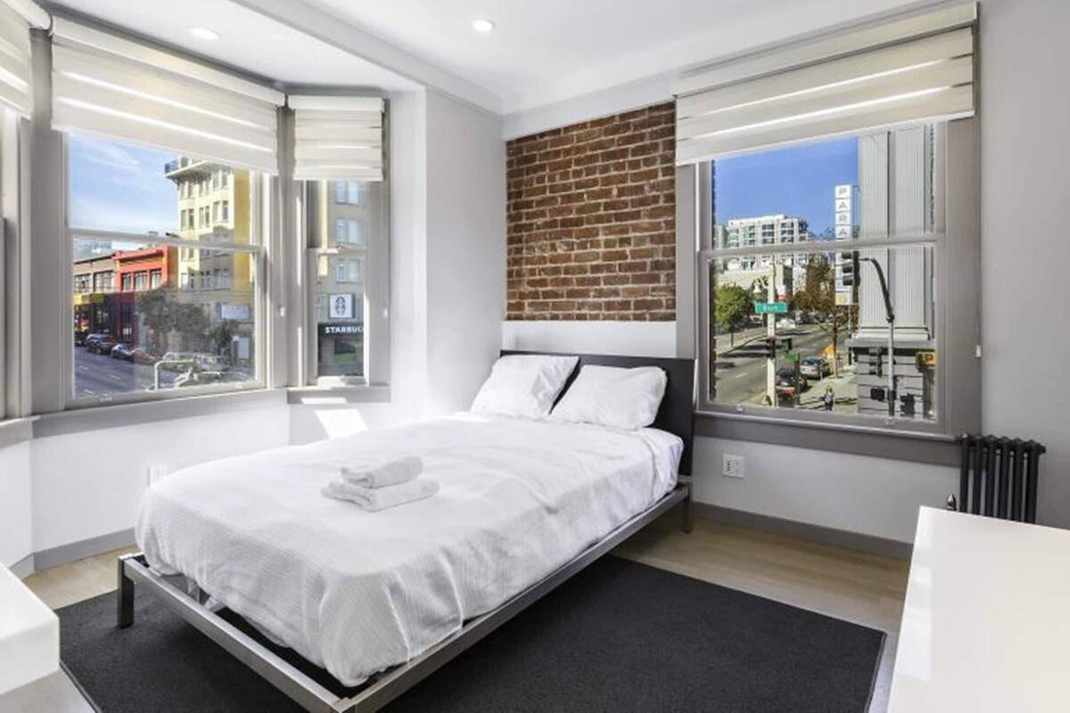 Ein modernes Hotelzimmer mit einem großen Bett, zwei Fenstern, einer Ziegelfassade und Blick auf die Stadt.