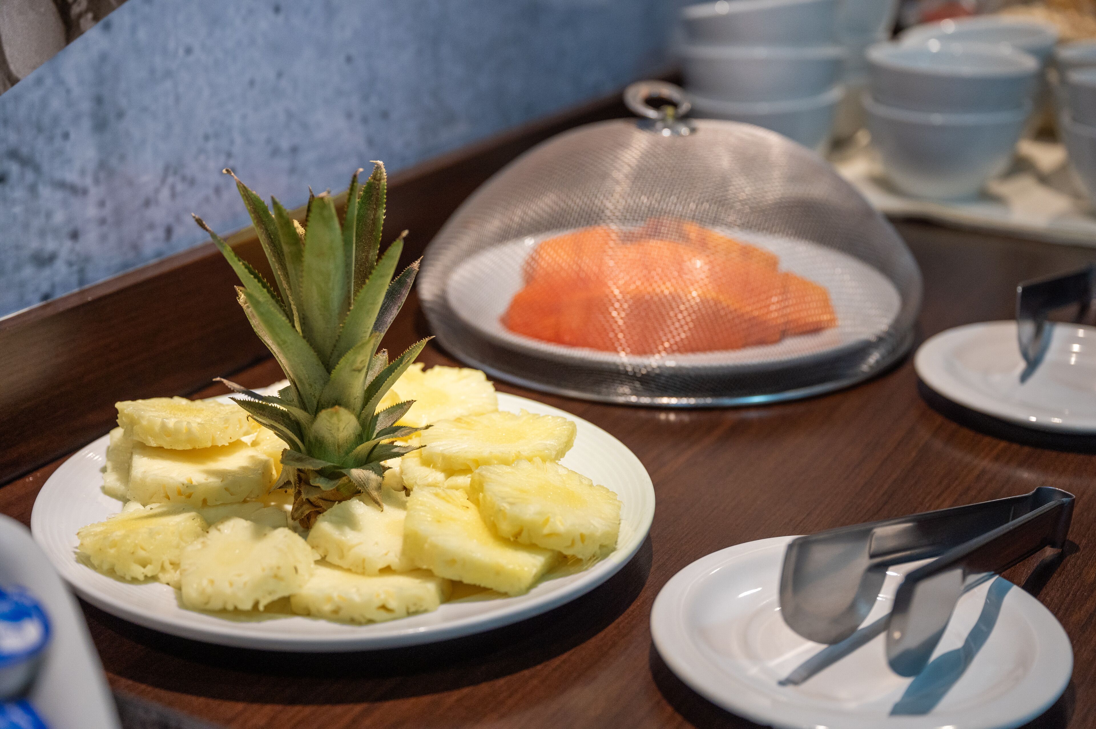 A breakfast buffet with plates of pineapple and orange slices, a pineapple centerpiece, and a covered dish.