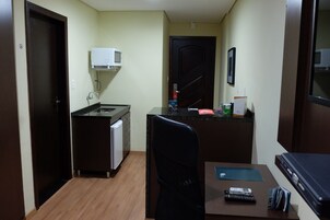 A compact kitchenette with a microwave, sink, and small refrigerator. There is a chair and a table with a remote control and a notebook.