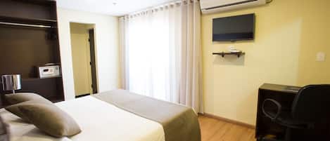 A hotel room with a bed, a desk, a chair, an air conditioner, a TV, and a bedside table.