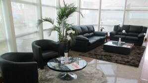 Un vestíbulo moderno con sofás de cuero negro, una mesa de centro de vidrio y una gran planta en maceta.