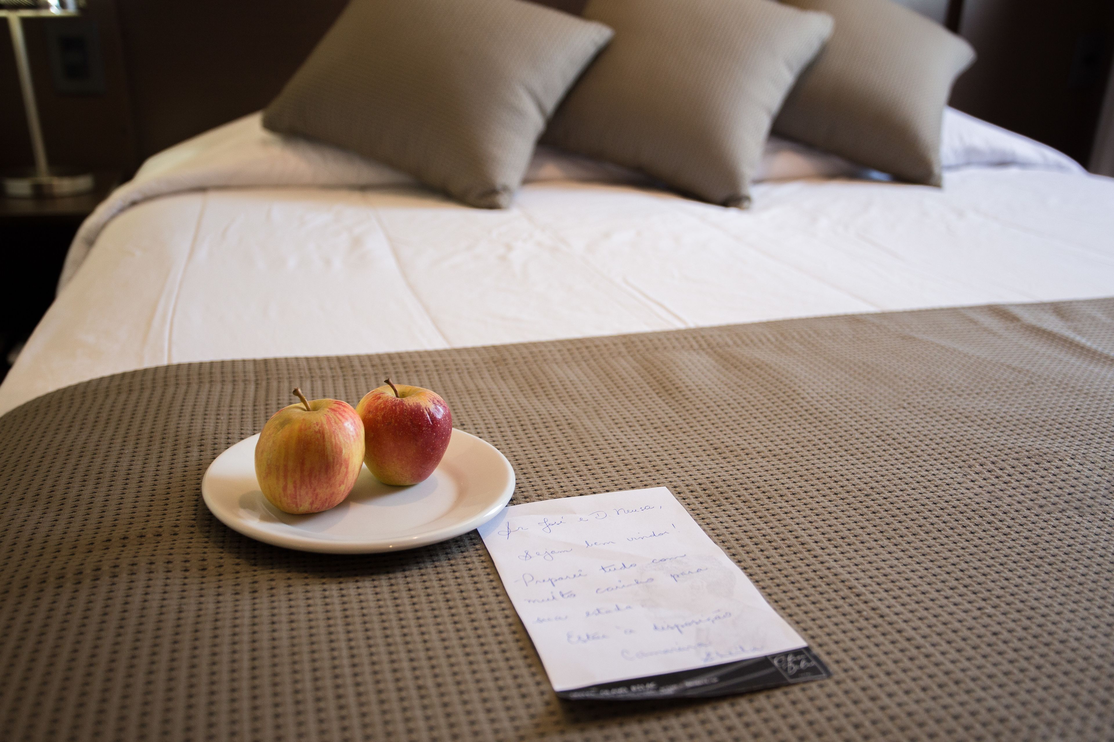 Una cama con almohadas, un plato con dos manzanas y una nota sobre la cama.