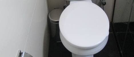 Et hvidt toilet med papirhåndklædeholder og en lille skraldespand ved siden af.