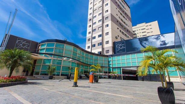 Un edificio moderno con fachada de vidrio curva, una amplia puerta de entrada y palmeras en primer plano.