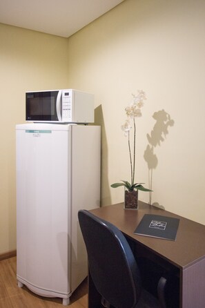 A compact room with a white refrigerator, a microwave on top, a small table with a chair, and a potted orchid. - Olavo Bilac Hotel (Taubate)