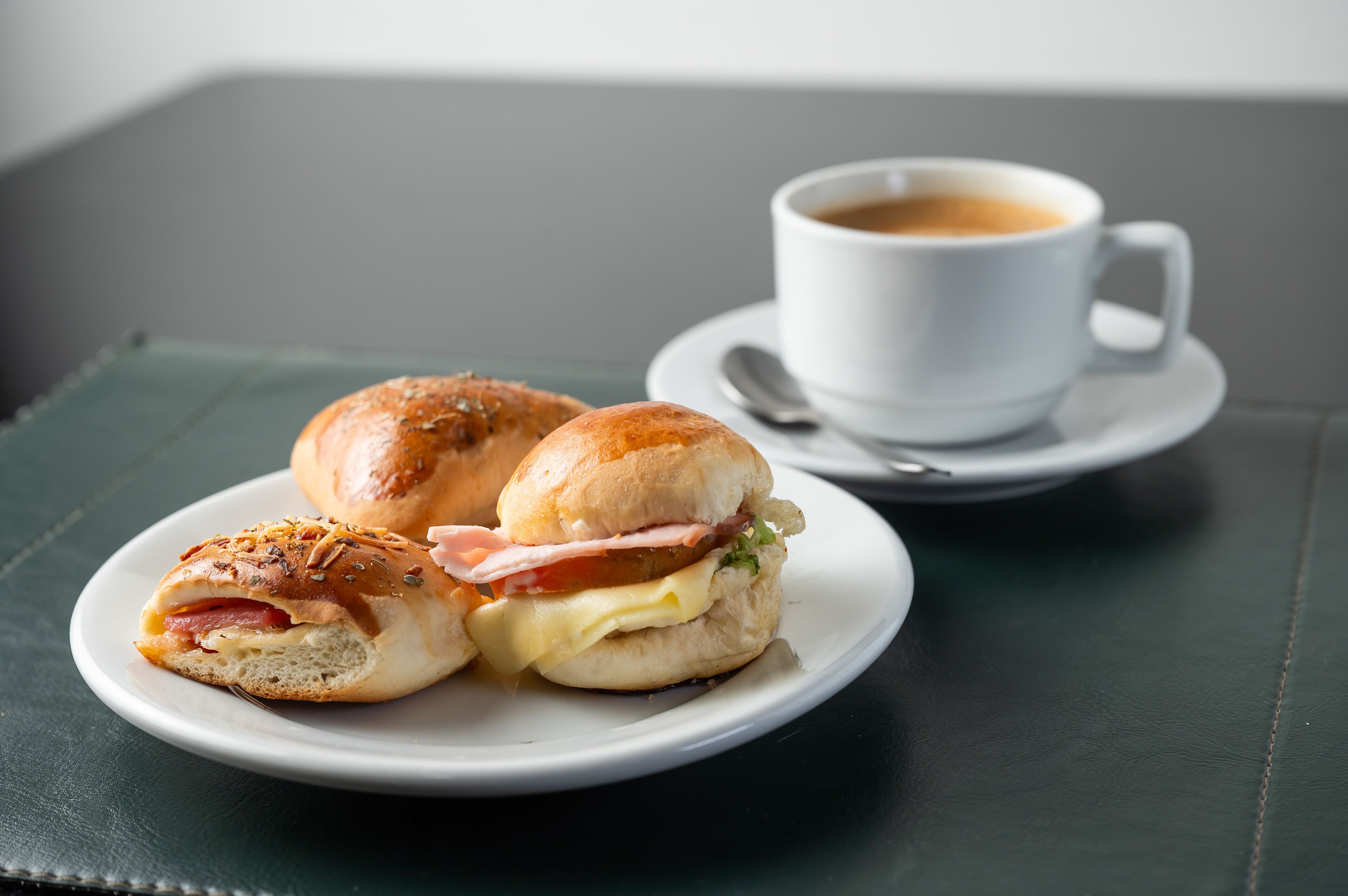 A sandwich on a plate with a cup of coffee in the background.