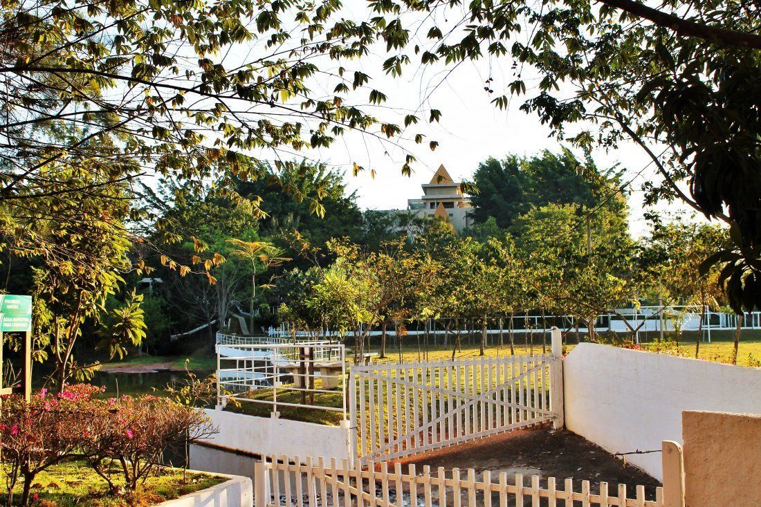 A gated area with a white fence, trees, and a building in the background.