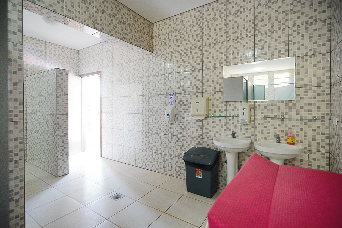 Ein Badezimmer mit gefliesten Wänden, zwei Waschbecken, einem Spiegel und einem Mülleimer.