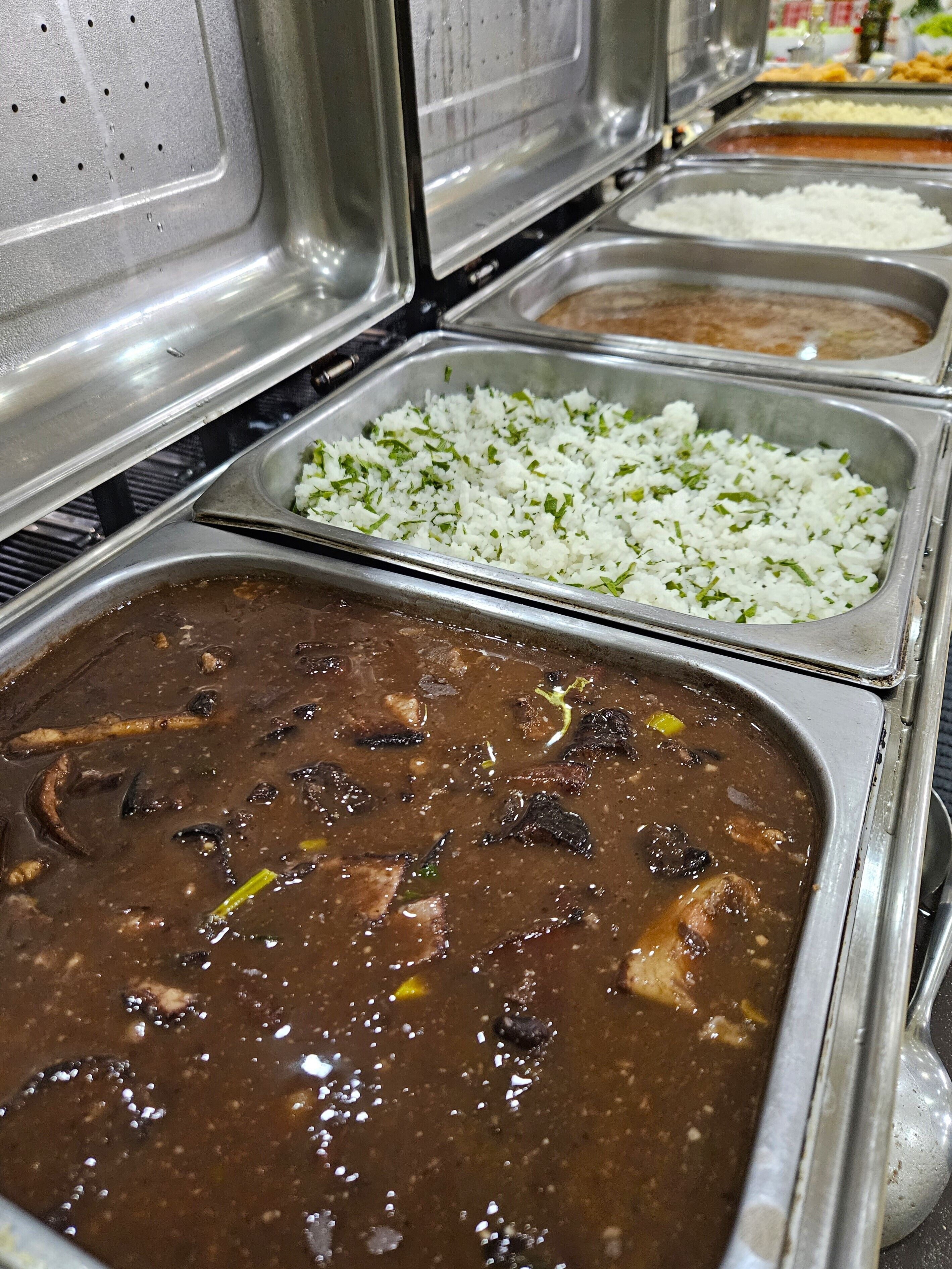 Un bufé con diversos alimentos, incluyendo arroz, un guiso oscuro y otros platos.
