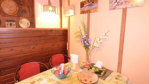 A dining area with wooden paneling, a table with a floral tablecloth, a vase with flowers, and wall art. - Fairy's Garden Chalet (West Kelowna)