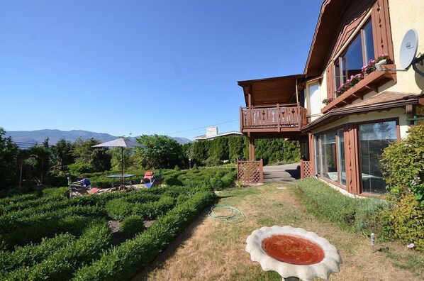 Una casa con balcón, un jardín con laberinto de setos y montañas al fondo.
