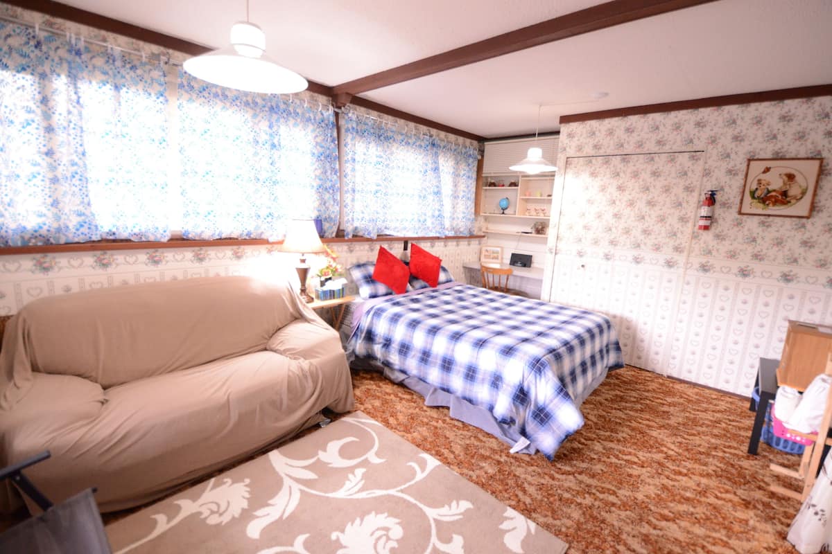 Een slaapkamer met een bed, een sofa, een bureau en een raam met gordijnen.