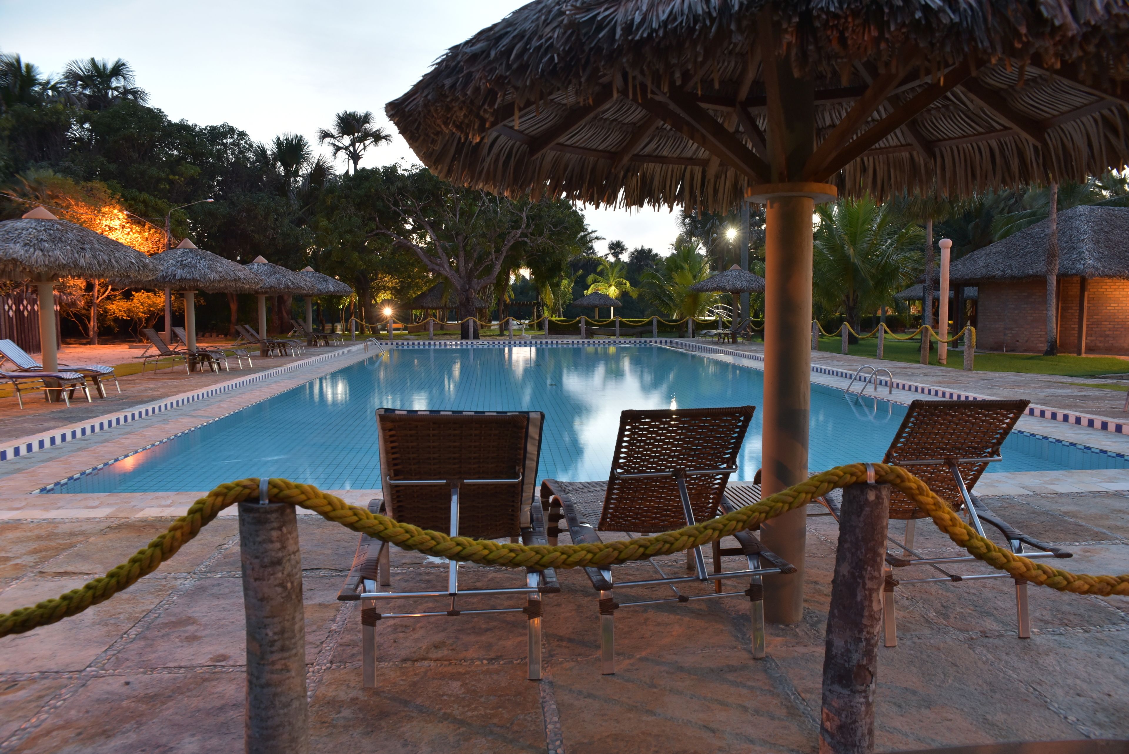 A pool area with lounge chairs and thatched umbrellas.