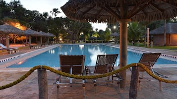 Un área de piscina con sillones de descanso y sombrillas de paja.