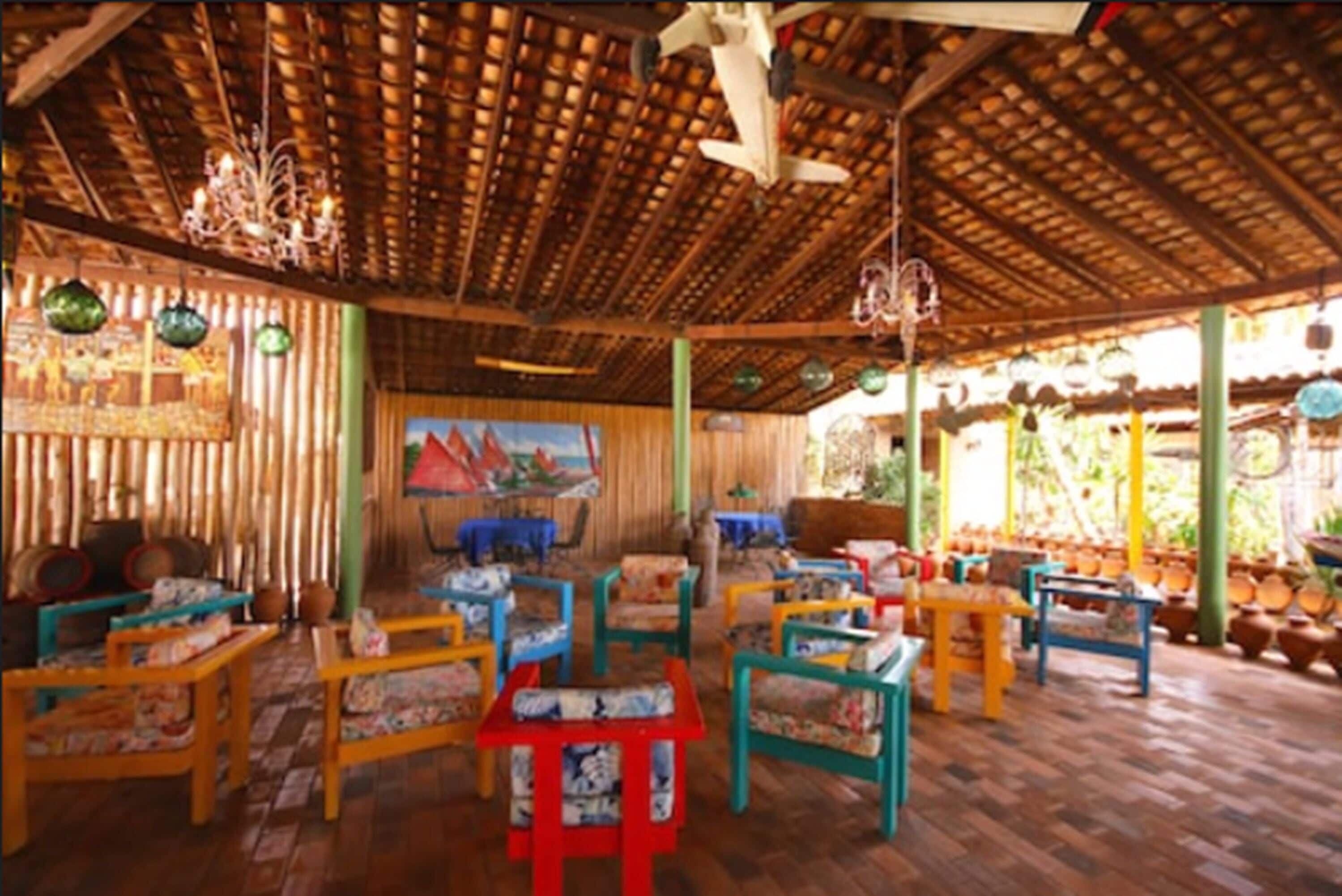 A covered outdoor seating area with colorful chairs and tables, a wooden floor, and a bamboo wall.
