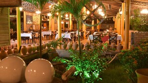 Un restaurante con mesas y sillas en su interior, rodeado de plantas en macetas y jarrones decorativos.