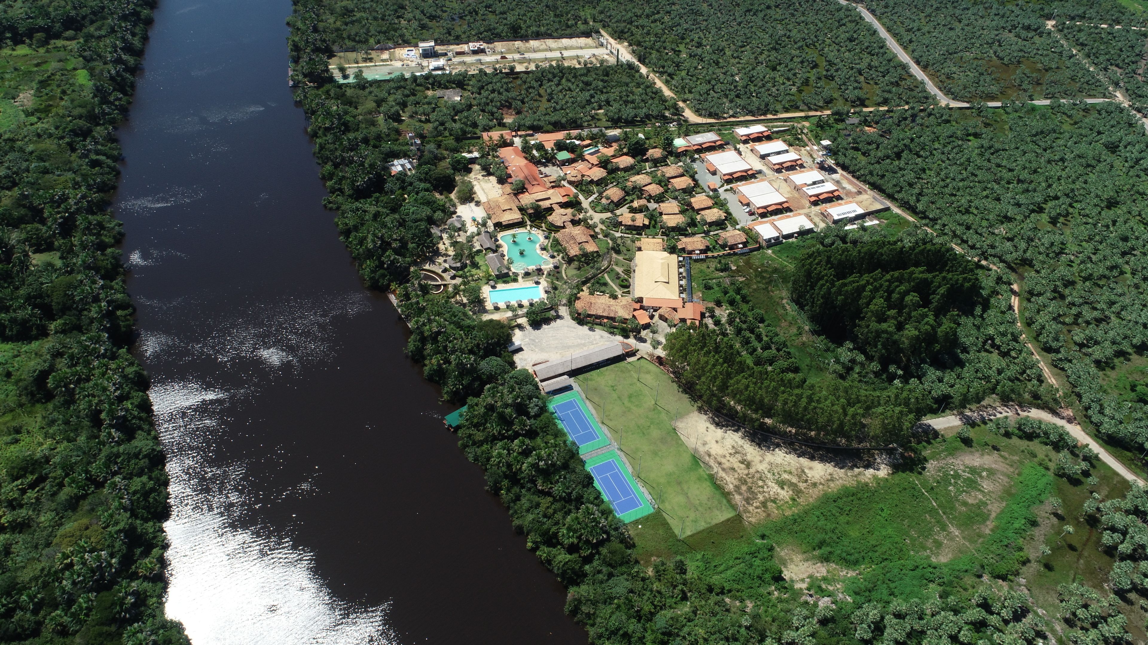 An aerial view of a resort with a swimming pool, tennis court, and multiple buildings.