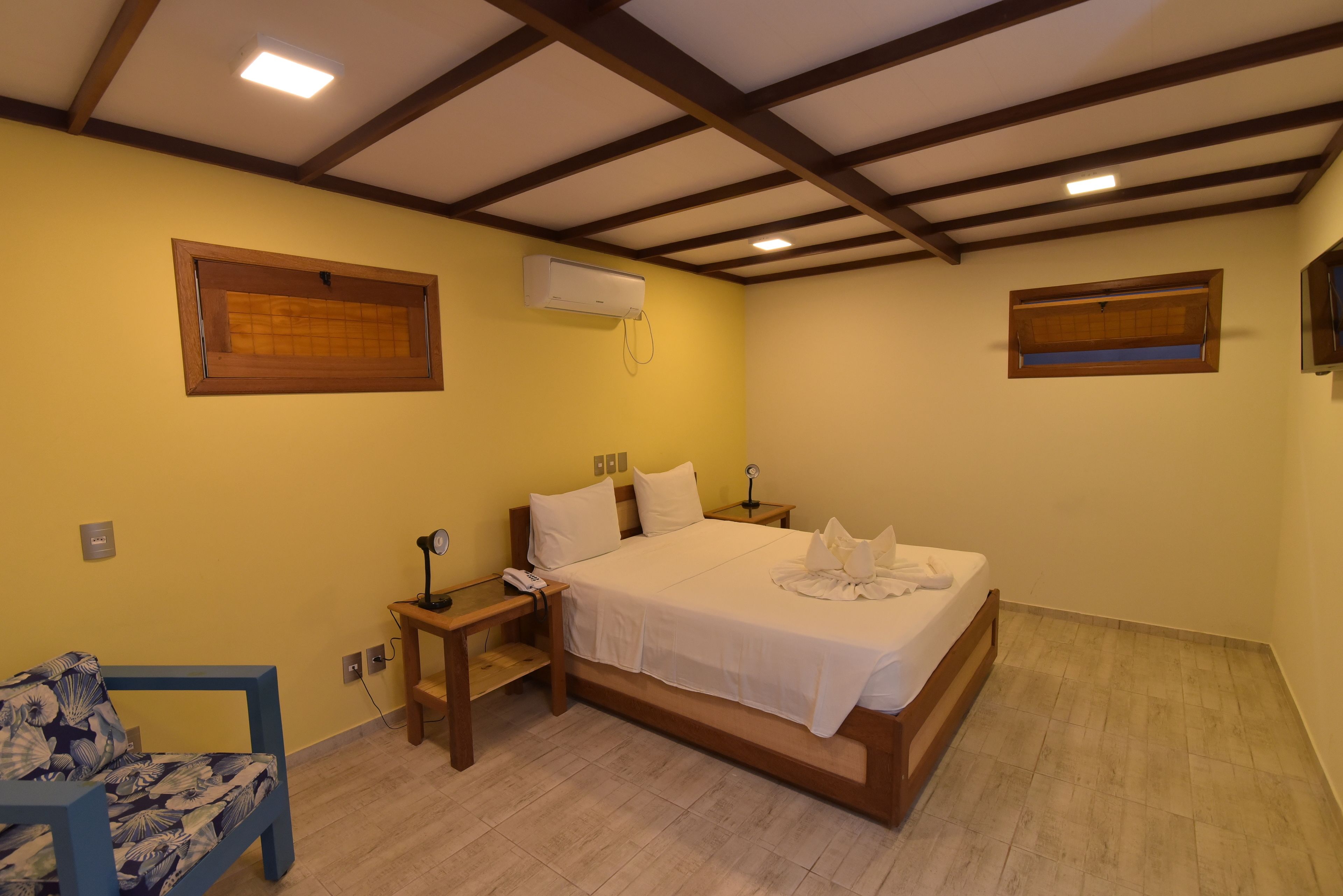 Un dormitorio con una cama, mesitas de noche, una silla y un aire acondicionado.