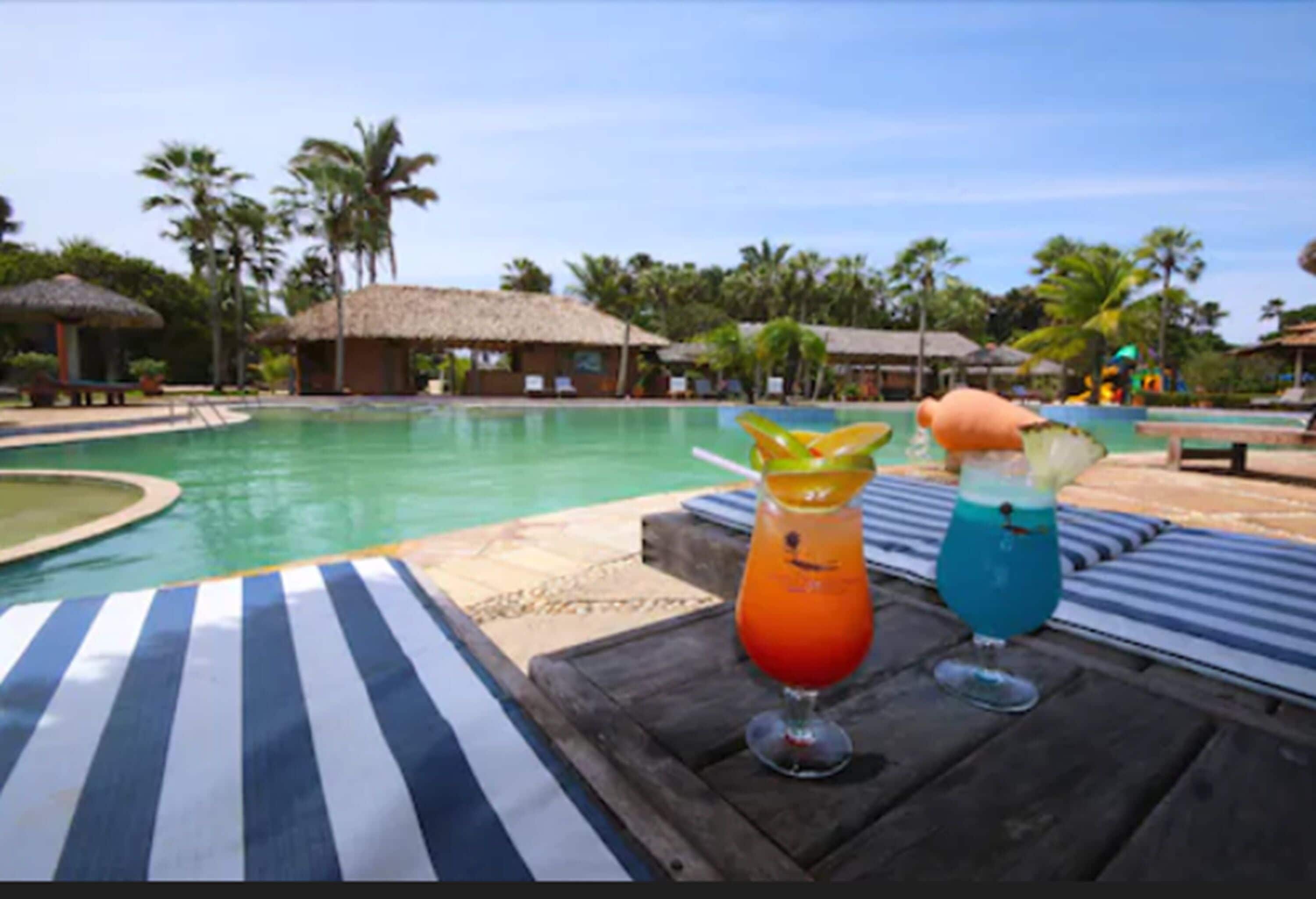 Ein Poolbereich mit Liegestühlen und zwei Cocktails auf einem Holztisch.