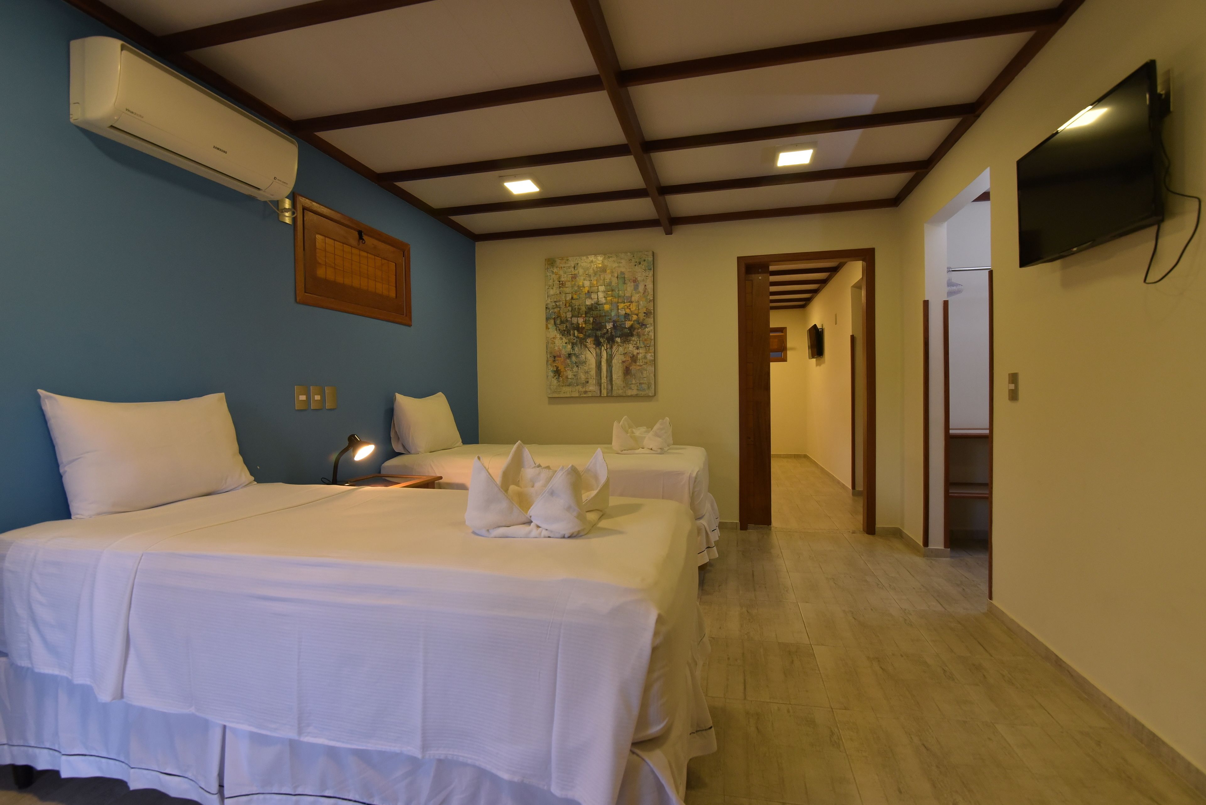 A hotel room with two beds, a flat-screen TV, an air conditioner, and a painting on the wall.
