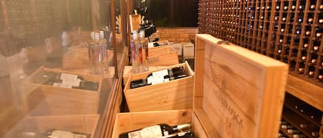 Ein Weinkeller mit Holzkisten voller Flaschen, einem Weinregal im Hintergrund und einer Backsteinwand.