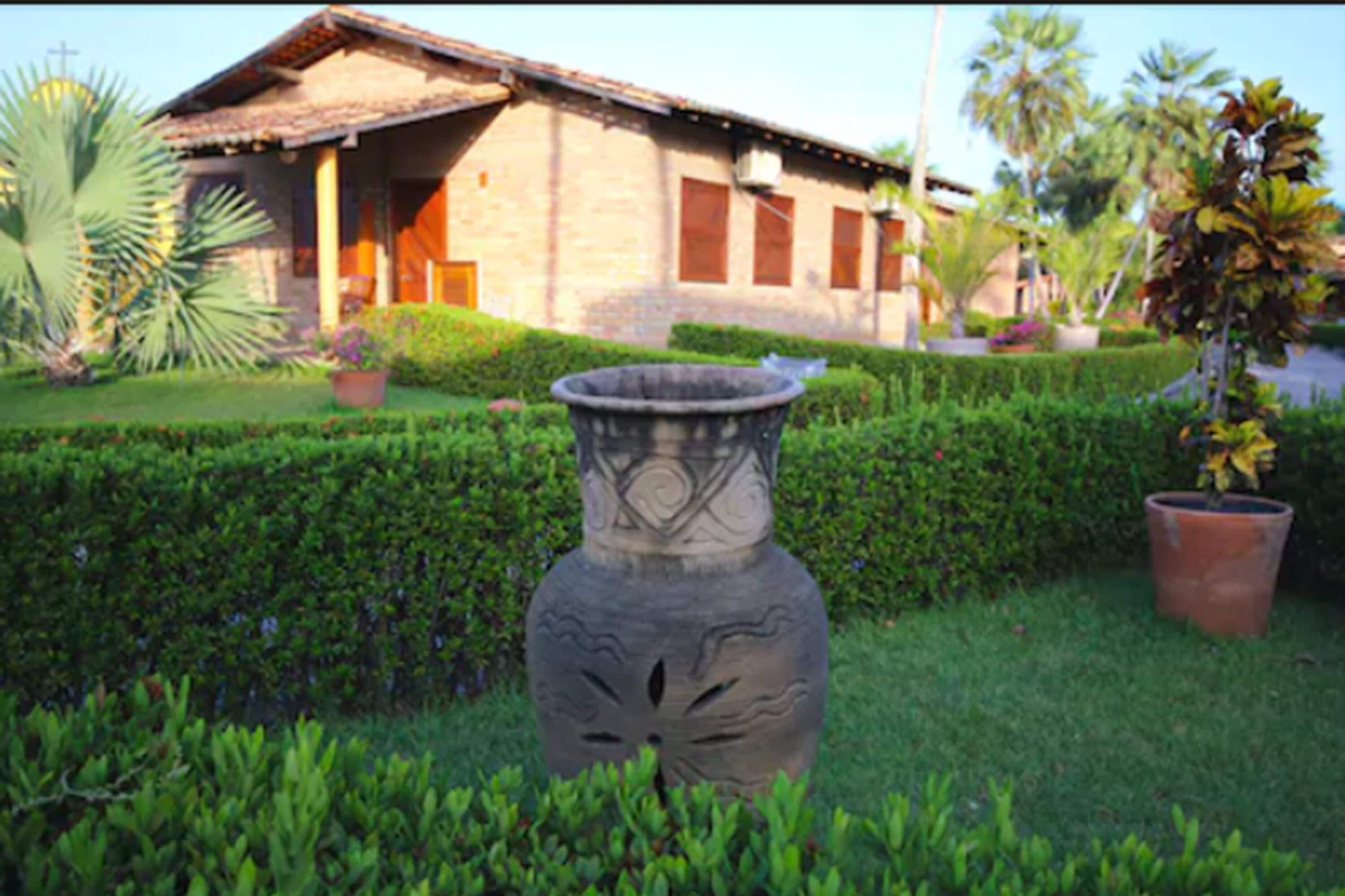 A house with a tiled roof, a front porch, and a garden with a large decorative vase.