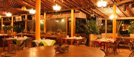 An indoor dining area with round tables and chairs, wooden beams, and hanging lights.