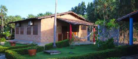 A rustic building with a tiled roof, a porch, and a fenced yard with potted plants.