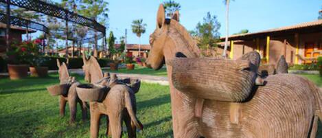 Escultura de un caballo y un burro en un jardín con palmeras y un edificio al fondo.