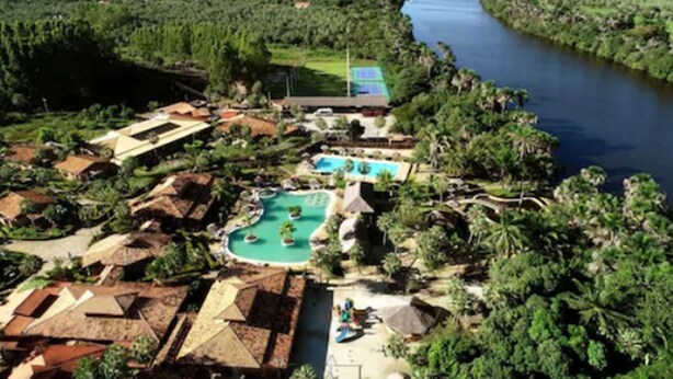 Vista aérea de un resort con piscina central, varias villas para huéspedes y un río.