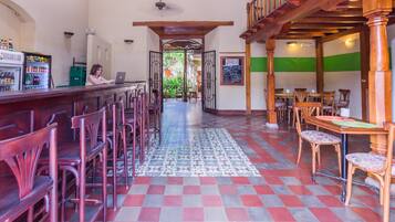 Uma área de bar com balcão, banquetas e piso estampado. Há mesas e cadeiras na área de jantar.