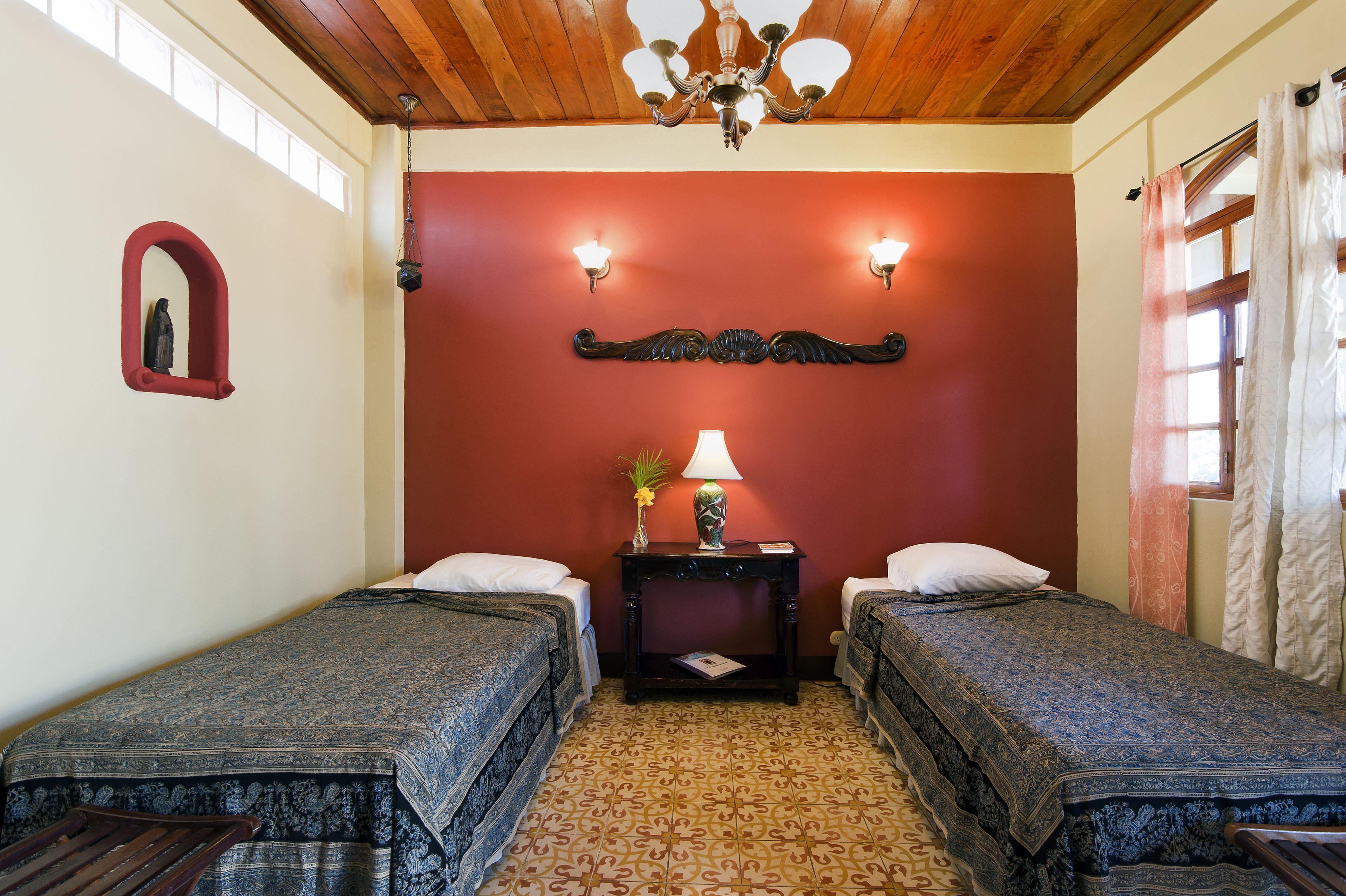 A room with two single beds, a small table with a lamp, and a decorative mirror on the wall.