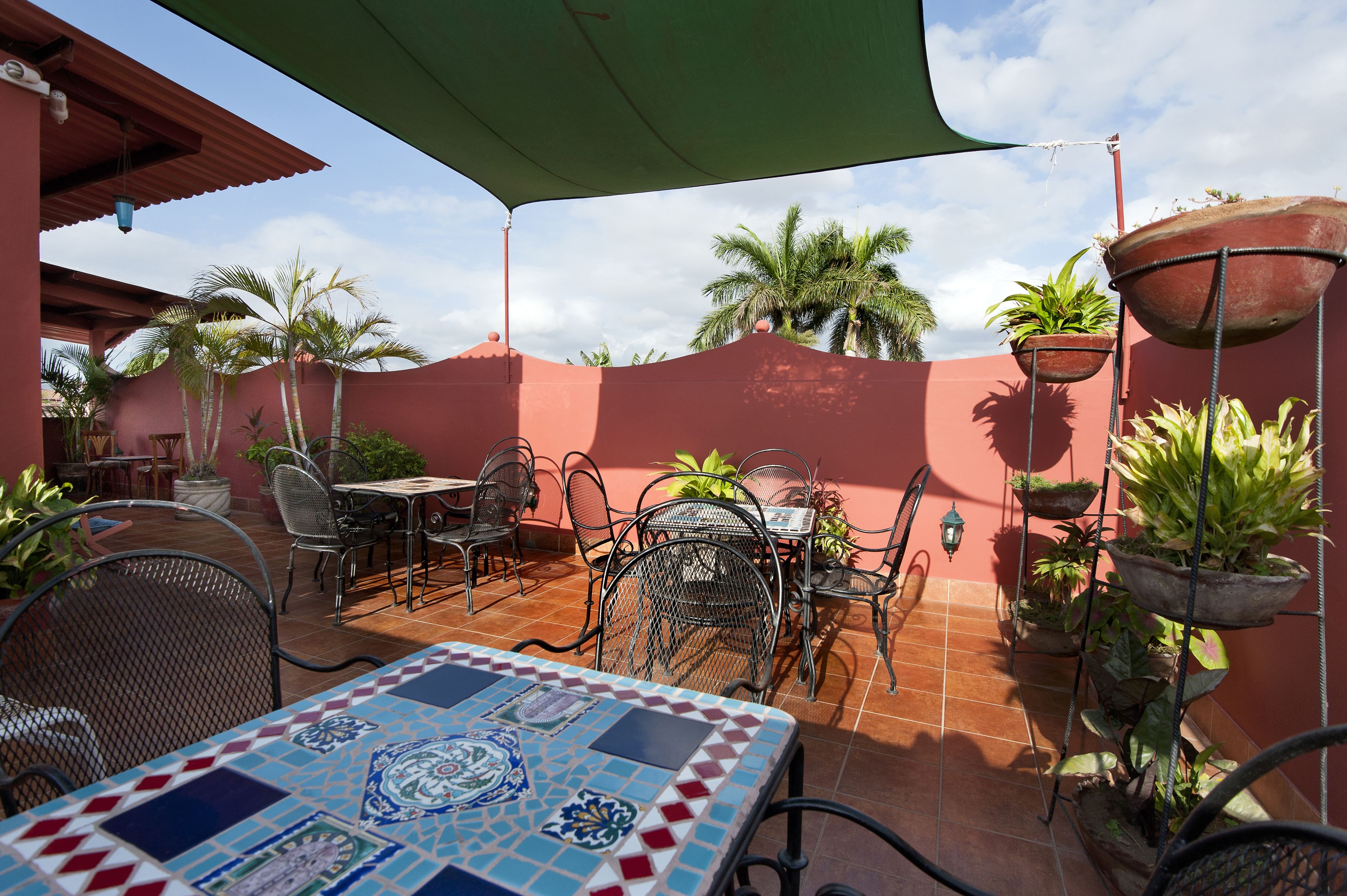 Un patio al aire libre con una mesa de baldosas, sillas de metal y plantas en macetas.