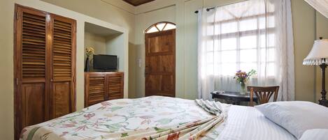 A bedroom with a floral bedspread, wooden wardrobe, a television, and a window with curtains.