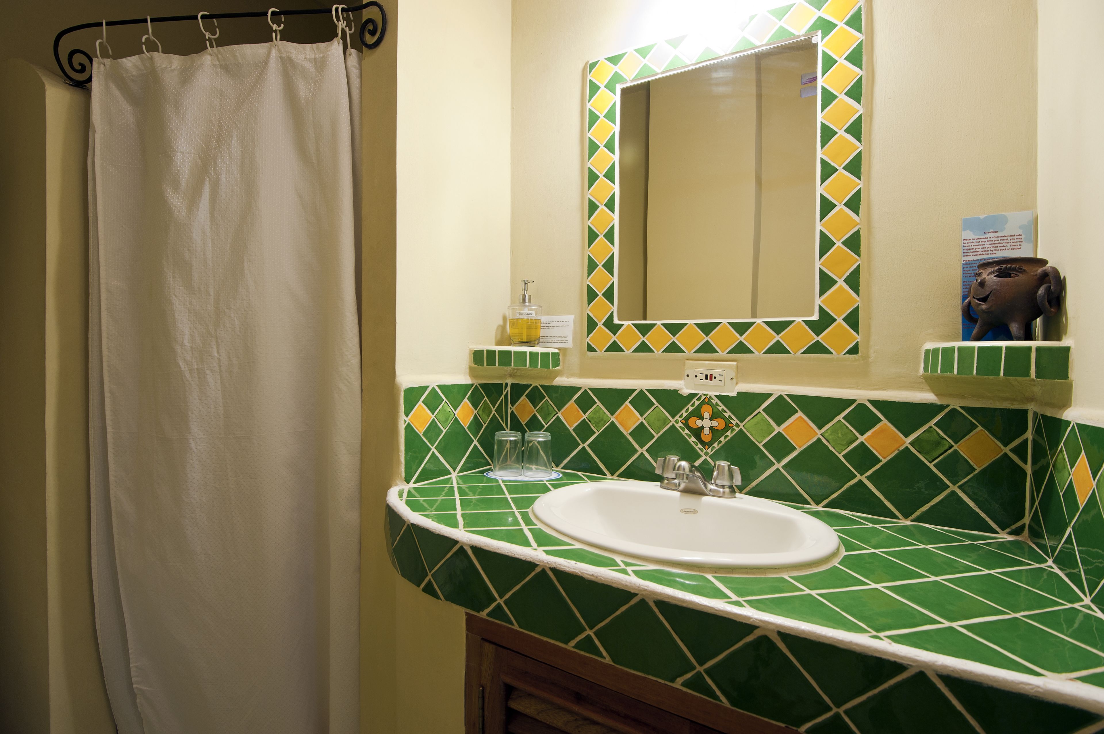 A bathroom with a green and yellow tiled wall, a white sink, and a mirror above it.