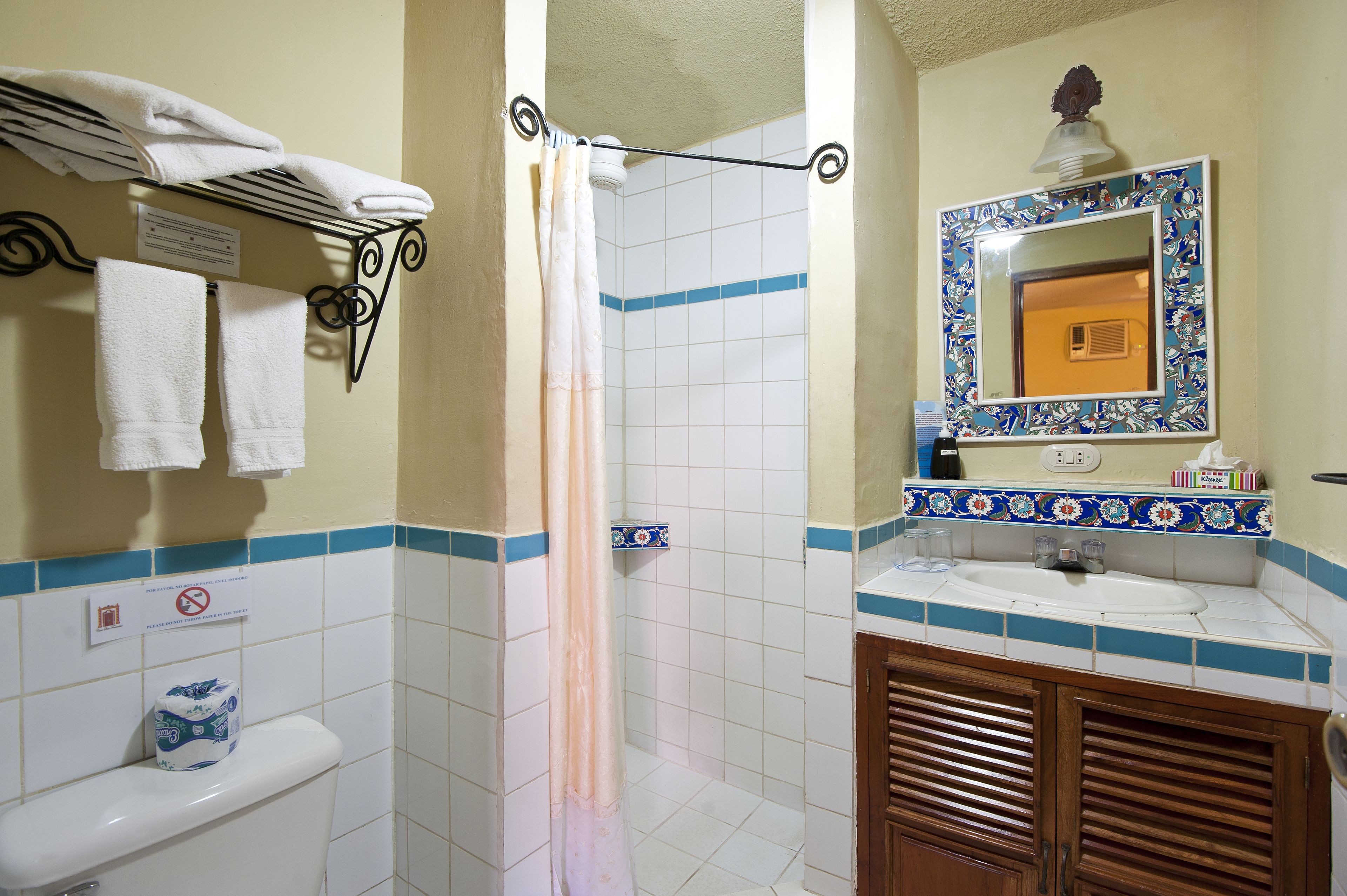 A bathroom with a toilet, sink, and shower. There are towels hanging on a rack, a mirror with a decorative frame, and a sign on the wall.