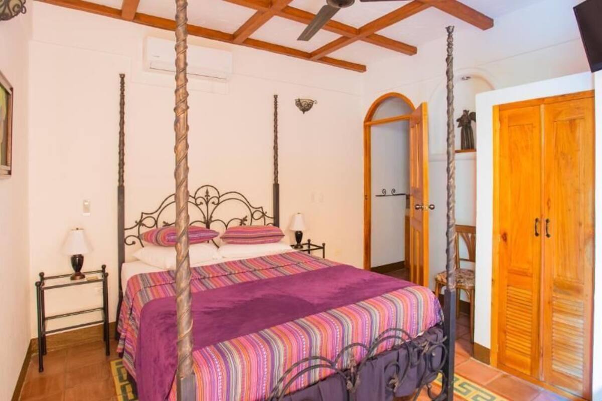 A bedroom with a four-poster bed, a wooden wardrobe, and a mirror.