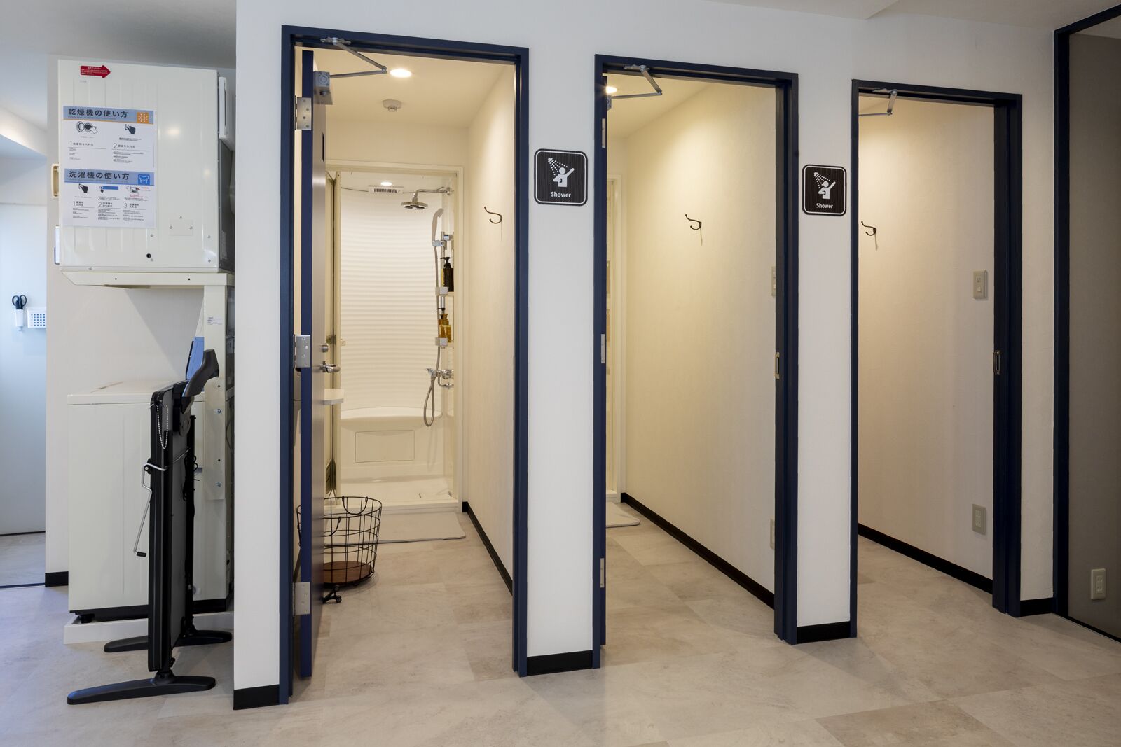 A hotel corridor with multiple doors, some marked with shower signs, and a visible shower room with a bathtub and shower head.