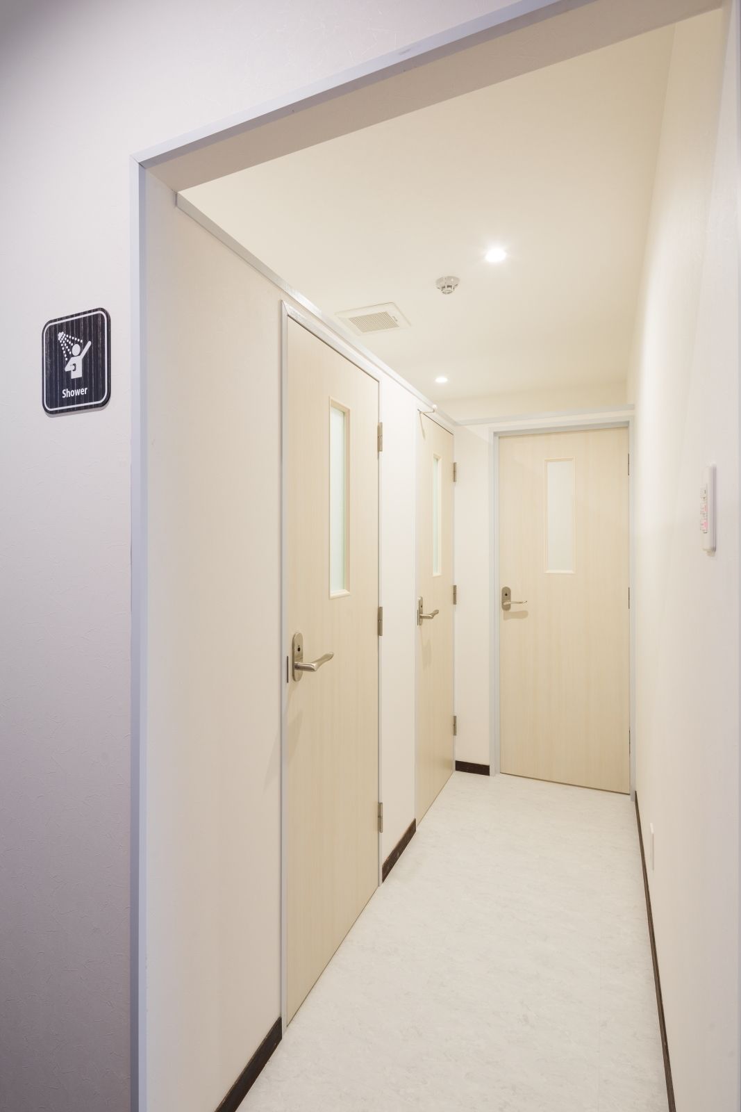 A narrow, well-lit hallway with three doors, one of which has a shower sign.