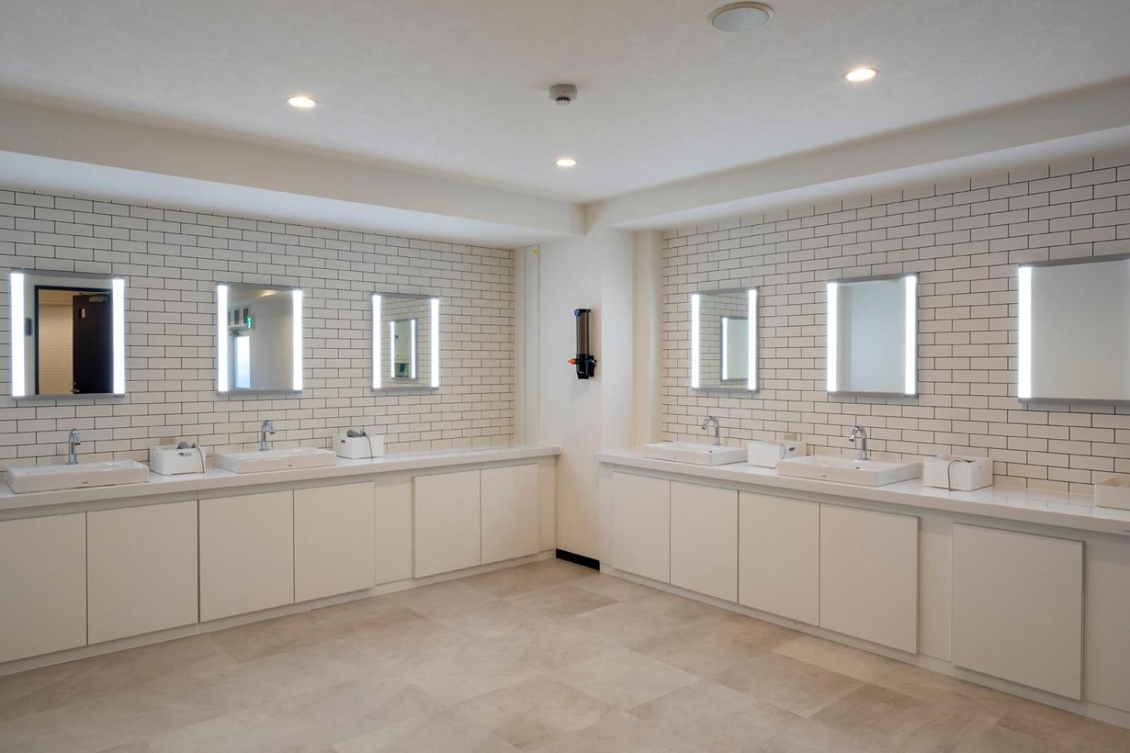 Un baño moderno con dos lavamanos, paredes de azulejos blancos y suelo de color claro.