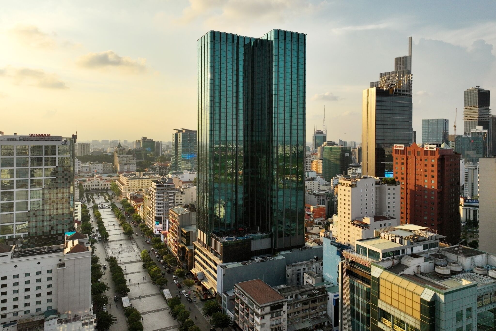 A high-rise building with a modern glass facade, surrounded by other buildings and a clear sky.